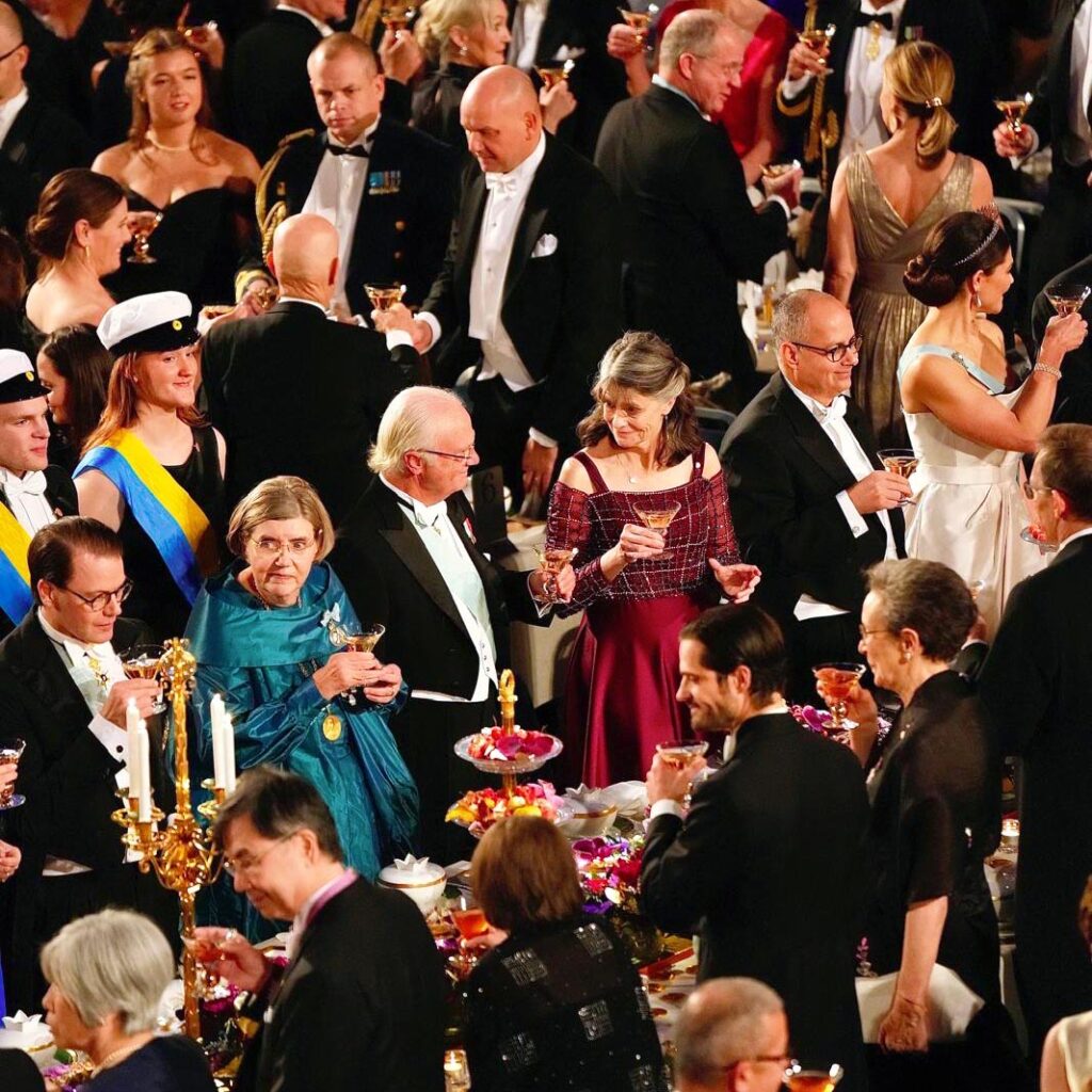 A bird's-eye photograph of a woman and man chatting while standing at a crowded formal dinner.
