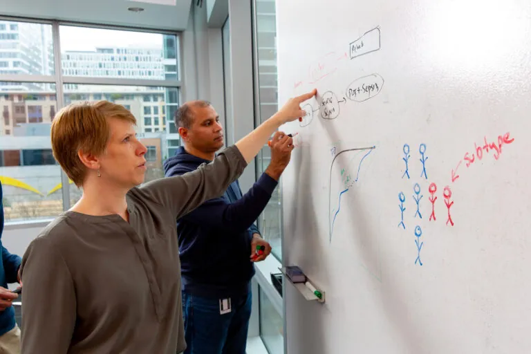 man and women solving an equation on a white board