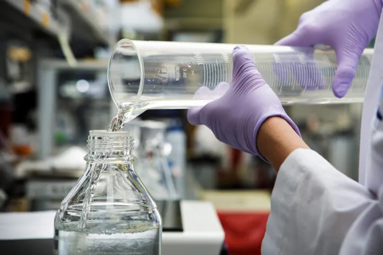 hands pouring liquid out of a beaker